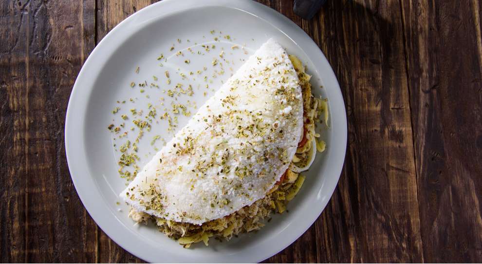 Crepioca recheada com frango servida em um prato branco redondo raso simples, em uma mesa de madeira.