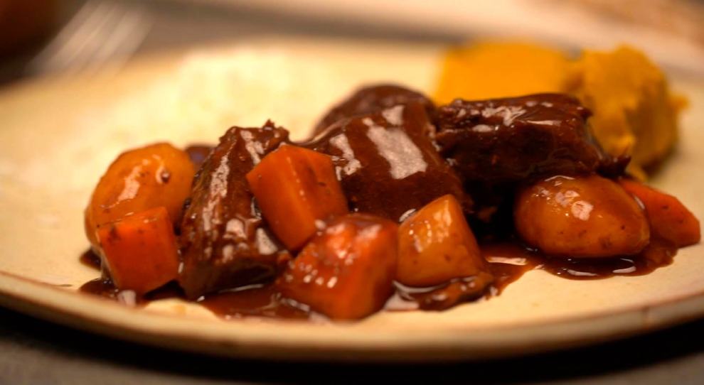 Imagem destaca a receita de carne de panela com legumes servida em um prato raso.