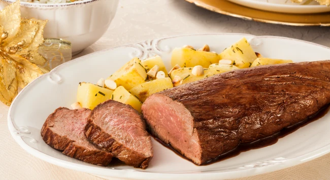 Rosbife de filé mignon servido com batatas em uma travessa de porcelana.