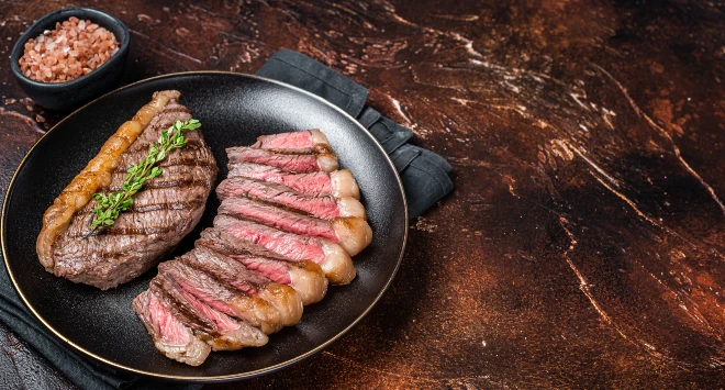 Bife de picanha grelhado, fatiado, servido em um prato redondo preto.