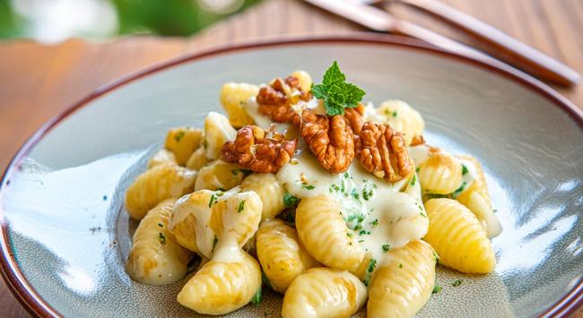 Nhoque de molho de queijo brie e nozes servido em uma porção em um prato branco e decorado com folha fresca.