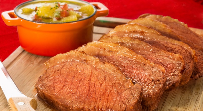 Fatias de picanha na manteiga servido em uma tábua de amdeira simples, com uma cumbuca de vinagrete de laranja ao fundo.