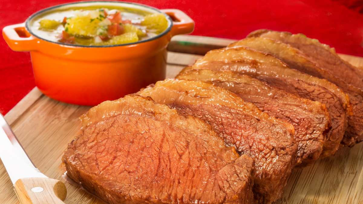 Fatias de picanha na manteiga servido em uma tábua de amdeira simples, com uma cumbuca de vinagrete de laranja ao fundo.