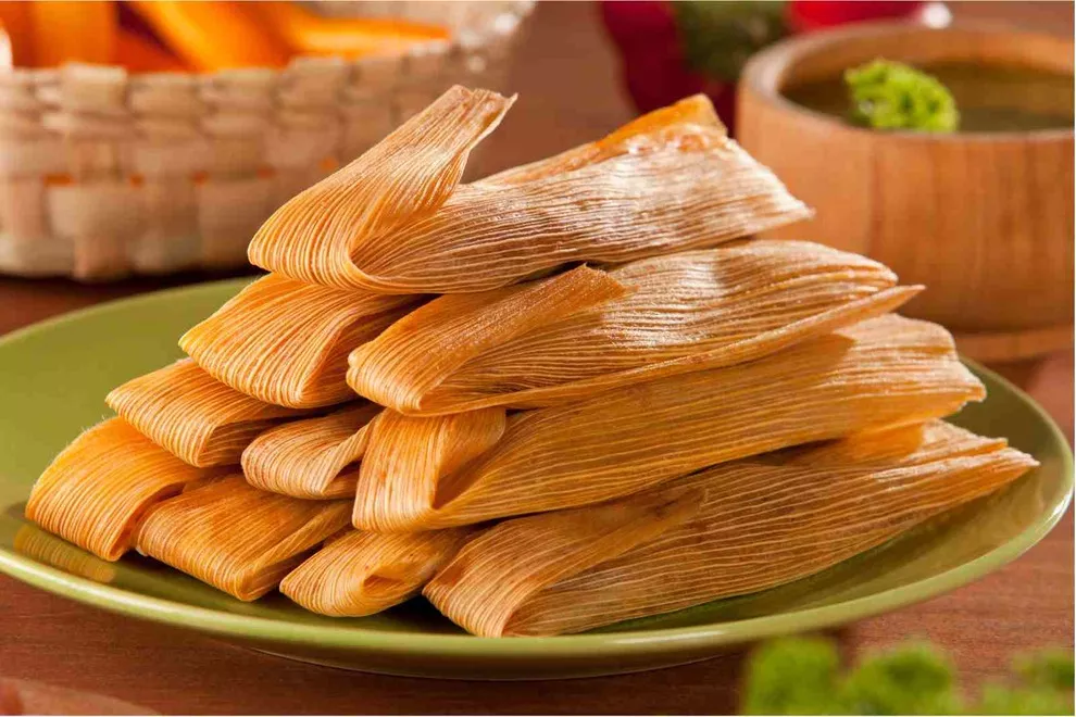 vários tamales em um prato verde encima da mesa de madeira