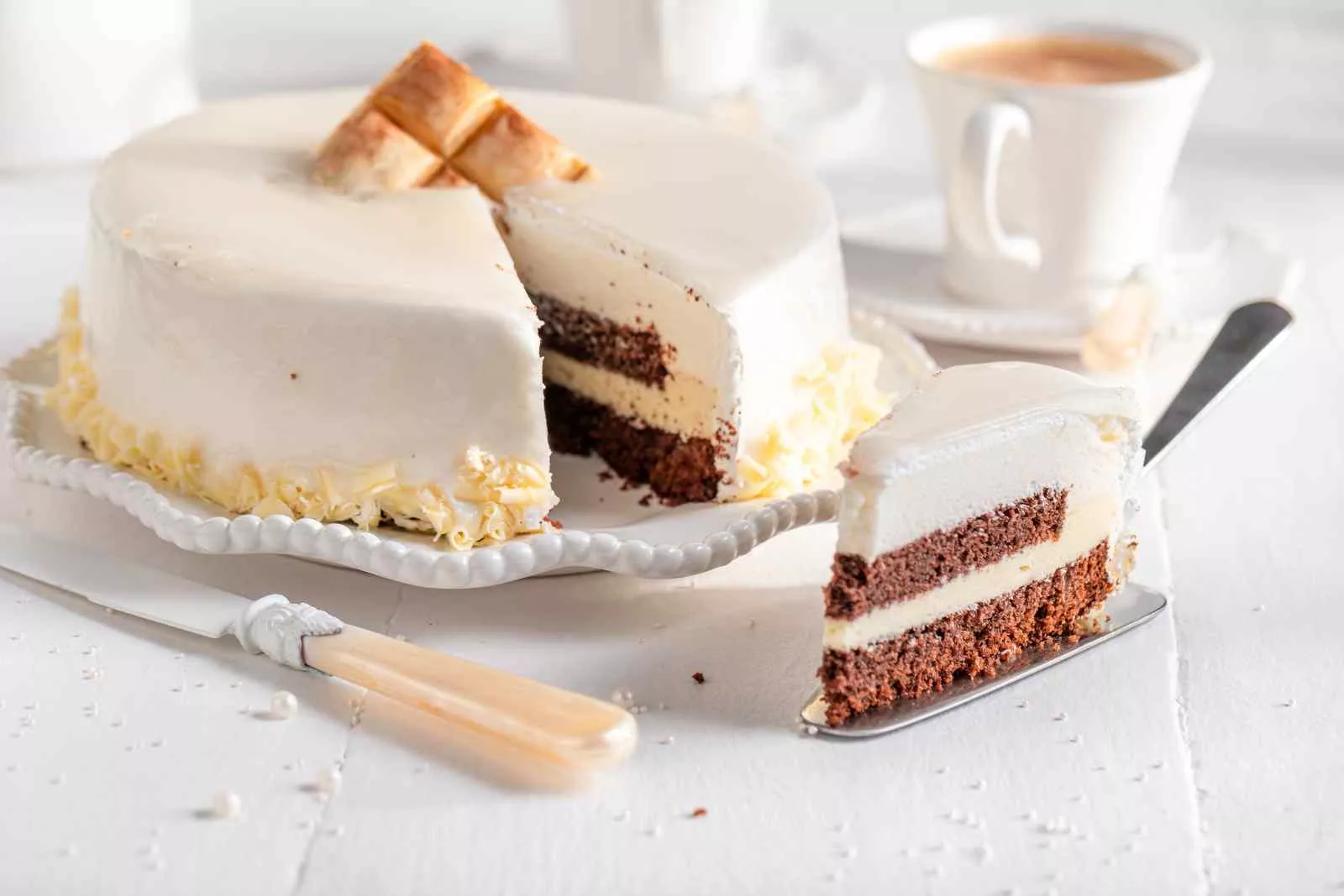 bolo de chocolate branco com uma xicara ao lado com uma fatia cortada