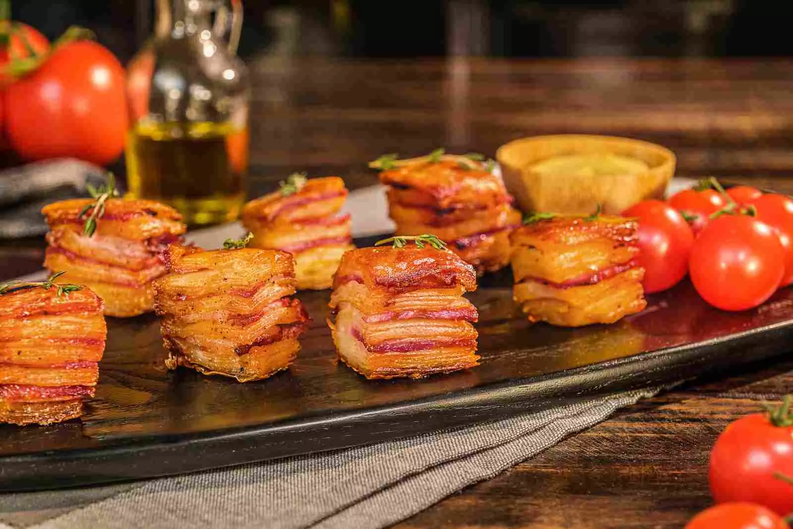 mil folhas de batata com bacon encima de uma mesa de madeira com vários tomates ao redor