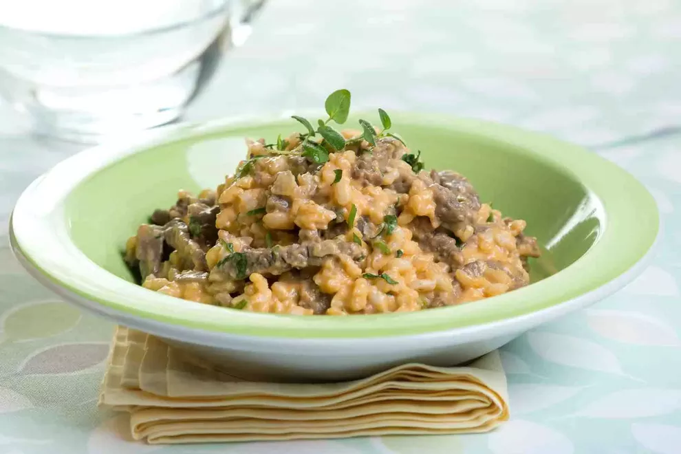 risoto de carne em um prato verde encima de uma mesa com pano em baixo do prato