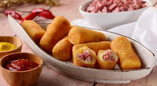 Bolinho croquete com recheio de mortadela em uma tigela em formato de peixe com molho ketchup e mostarda