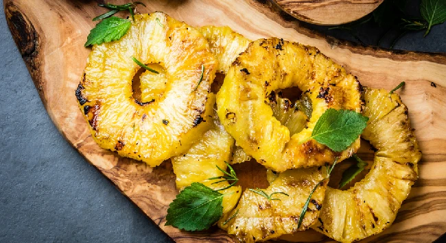 Fatias de abacaxi caramelizado em cima de uma tábua de madeira clara.