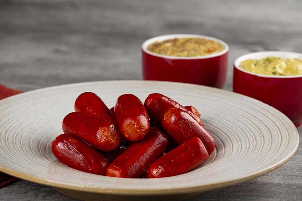 Diversos Kalbsbratwurst em cima de um prato redondo fundo, sob uma mesa de madeira.