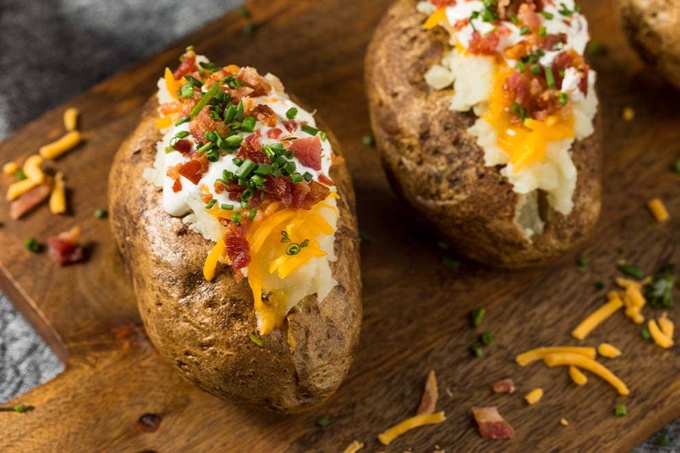 Duas unidades de Batatas recheadas em cima de uma tábua de madeira.