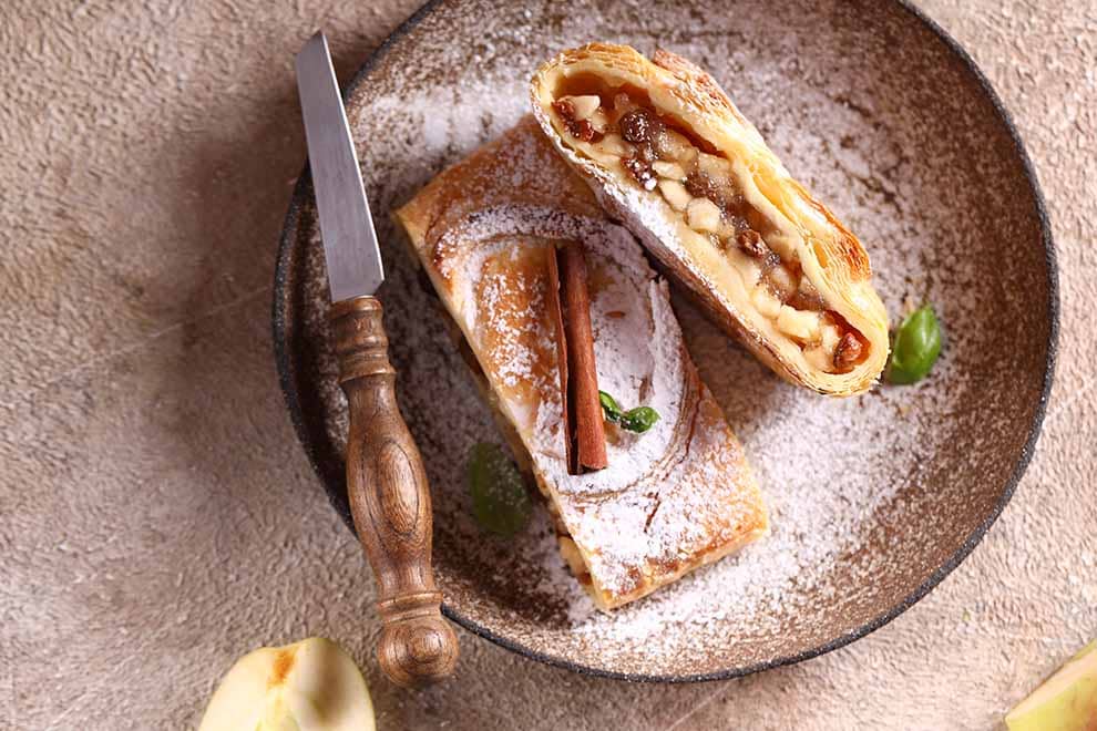 Duas unidades de Strudel em cima de um prato redondo bege, com uma espatula ao lado, sob uma uma mesa.