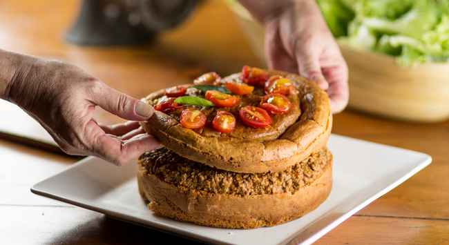 Torta mexicana de carne desfiada servida em um prato quadrado branco com tomates cerejas por cima da massa.