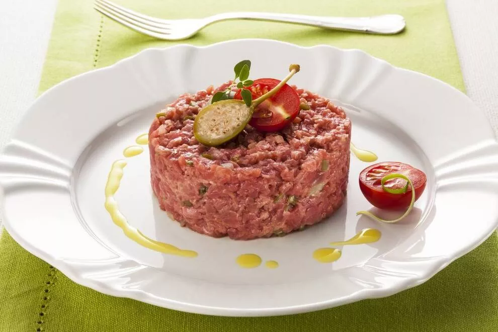 Prato branco com steak tartare dentro, em cima de uma mesa com toalha verde