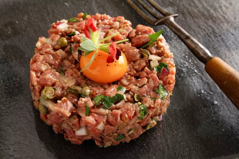 steak tartare na mesa com ovo encima com garfo ao lado