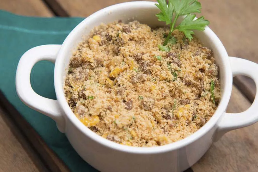 Farofa de alho em um pequena combuca branca, sob uma mesa de madeira.