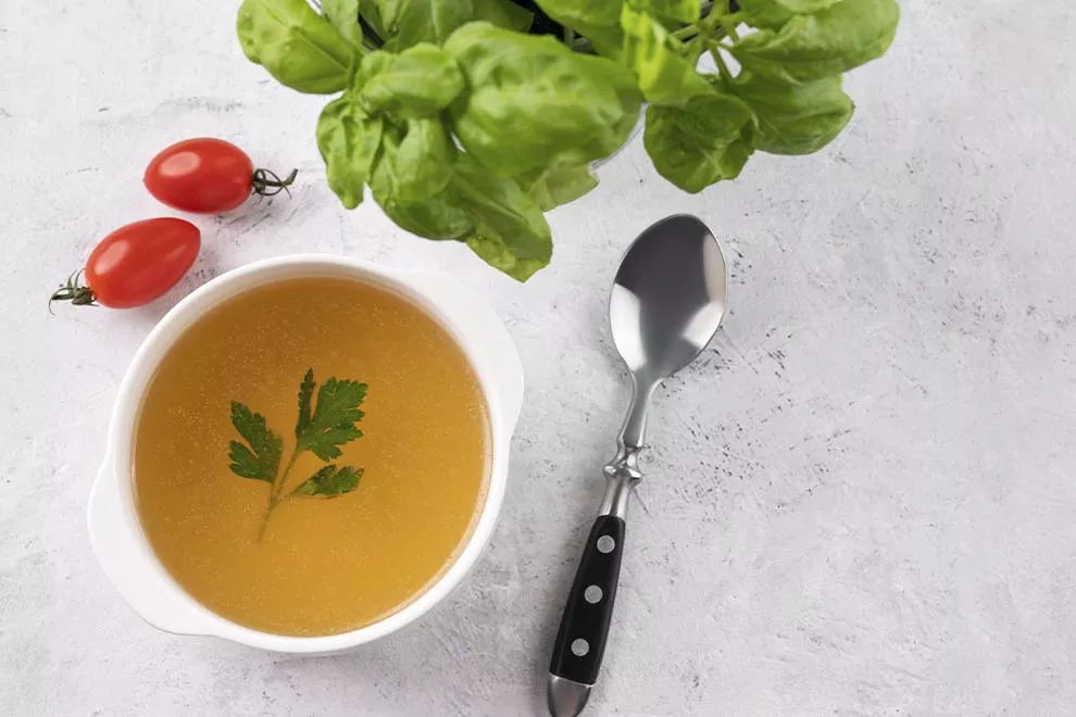 Caldo de carne com salsa em uma tigela branca sobre um fundo claro com ervas frescas e colher