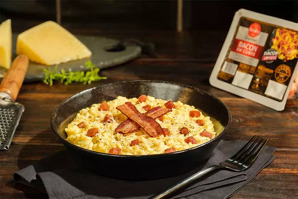 risoto á carbonara dentro de uma tigela preta com garfo ao lado e em cima de um pano preto, em cima da mesa de madeira escura