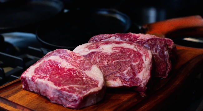 Bifes de entrecote dispostos em uma tábua de madeira de churrasco.