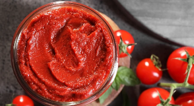 Extrato de tomate em uma tigela transparente com tomates pequenos em ramo ao lado.