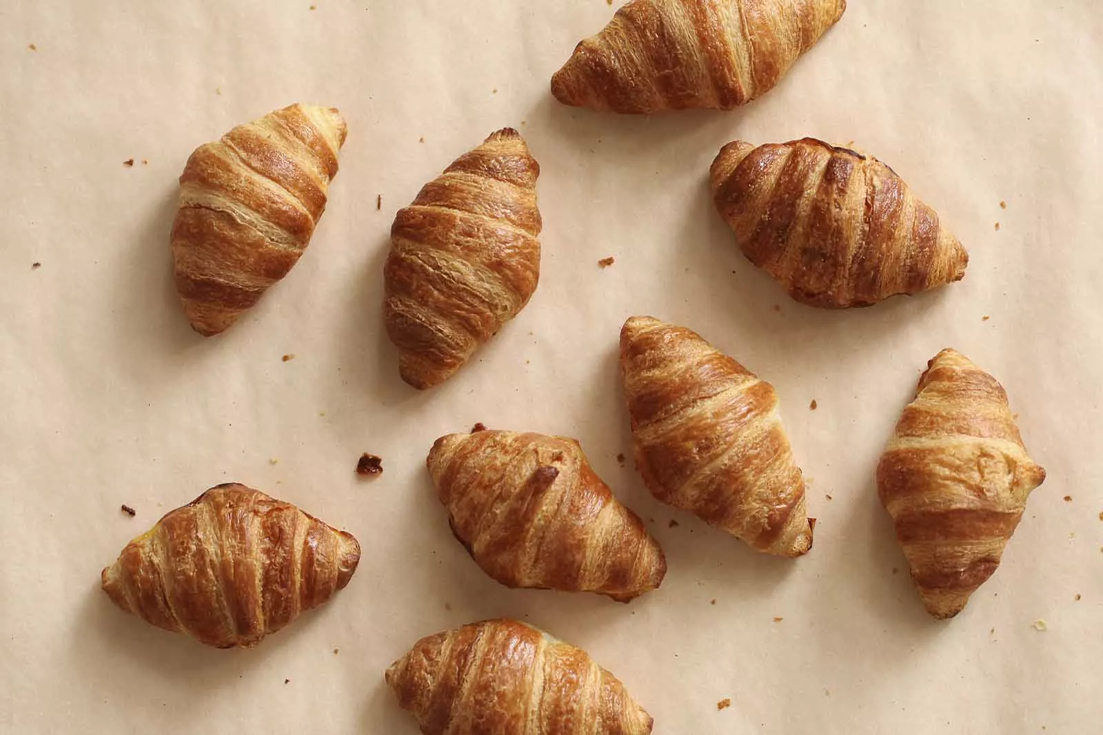 Imagem de diversos Croissants sob uma mesa marrom claro, vistos de cima 