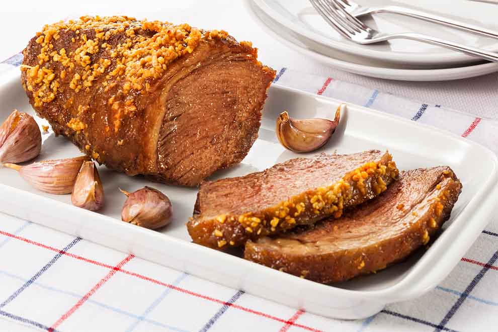 picanha a alho dentro de uma travessa branca de porcelana em cima de um pano branco em xadrez de azul e vermelho em cima de uma mesa