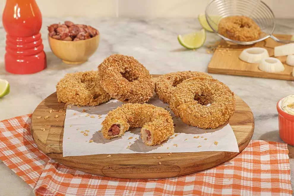 Diversas Onion rings recheadas com linguiça,  em cima de uma tábua de madeira redonda, sob uma mesa de mármore.