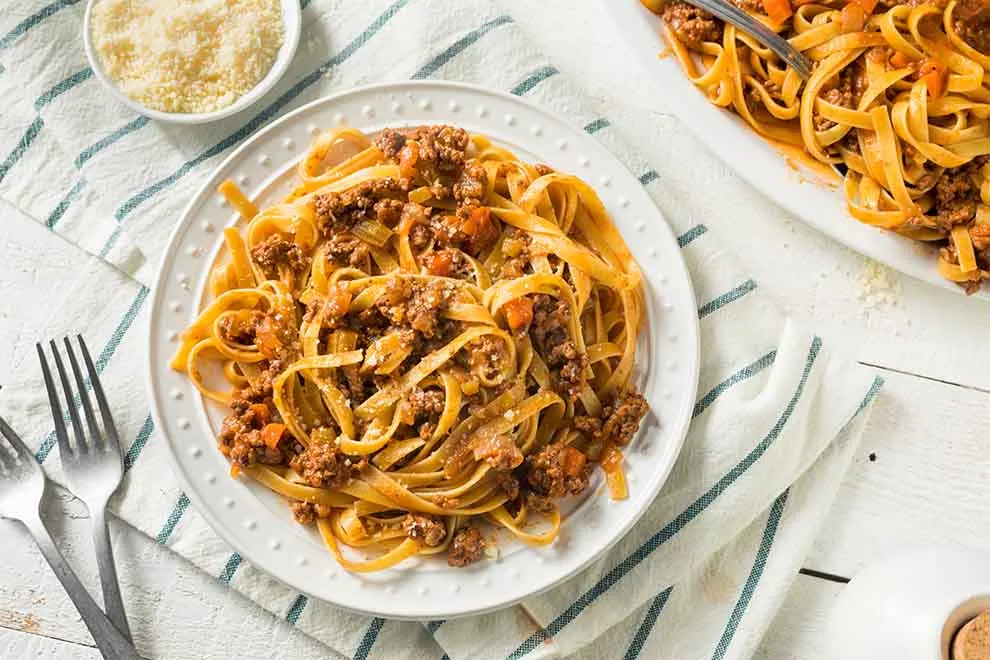 macarrão de rangu de carne dentro de um prato branco de porcelana em cima de um pano branco listrado em azul em cima de uma mesa