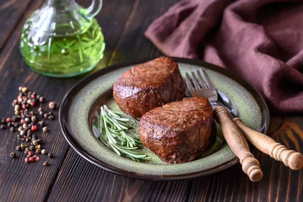 filé mignon em um prato verde com alecrim e azeite na mesa de madeira