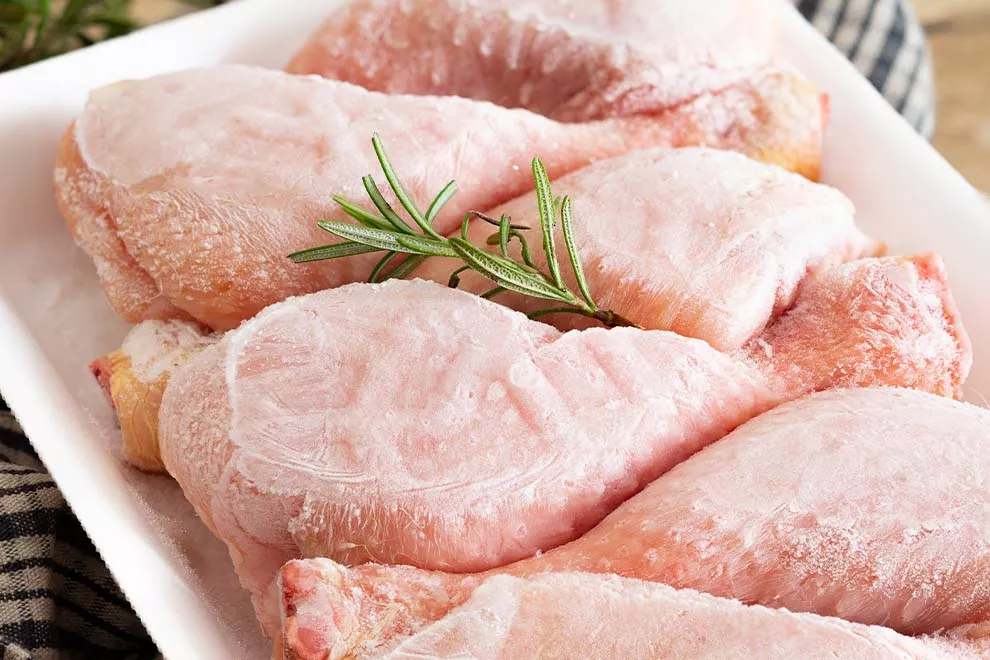 Coxas de frango congeladas em isopor, sob uma mesa de madeira 