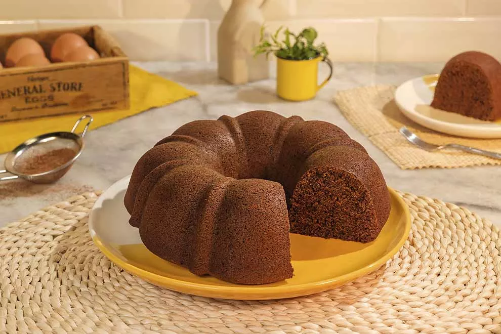 Imagem de um bolo de chocolate em cima de um prato redondo amarelo, com uma fatia dele faltando, sob uma mesa de mármore 