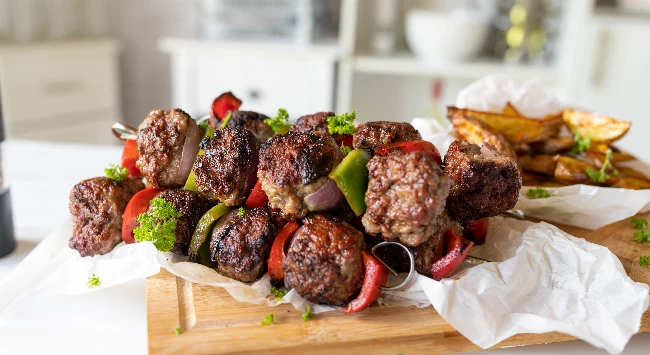 Espetinhos de almôndega com fatias de legumes empilhados em uma tábua de madeira de churrasco