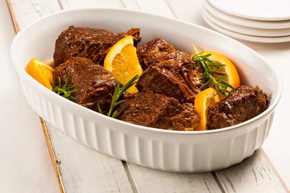 costela bovina em uma tigela branca com laranjas e alecrim juntos em uma mesa de madeira