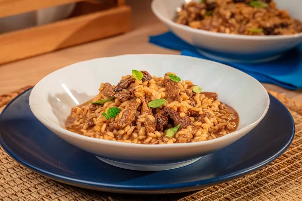 risoto de filé mignon em um prato branco com um tigela azul em baixo encima de uma mesa