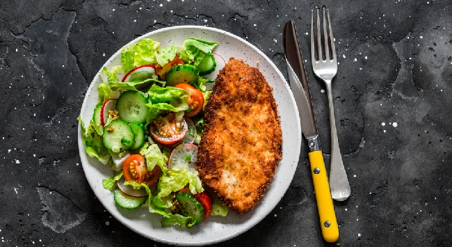 Bife à milanesa com salada verde e tomates em um prato. 