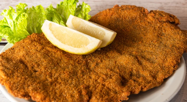 Bife à milanesa frito e servido com limão em uma travessa.