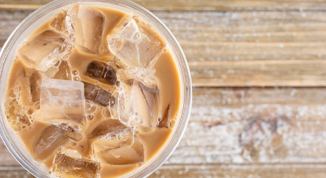 Copo com café gelado proteico servido em uma mesa de madeira.