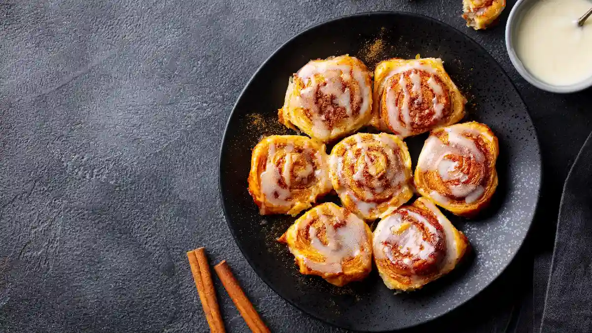 7 cinnamon roll servidos com leite condensado em um prato preto e redondo.