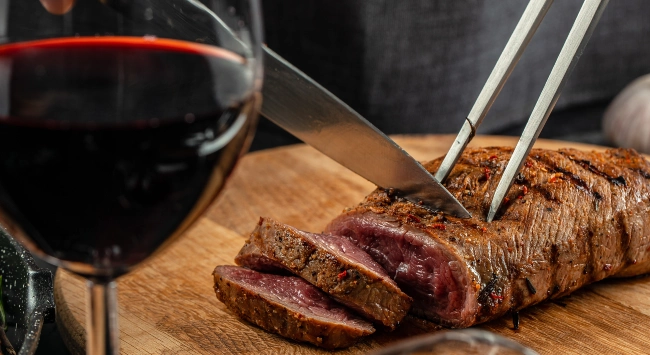 carne suculenta sendo fatiada e servida com uma taça de vinho.