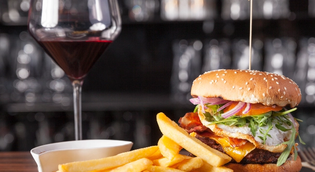 Um lanche completo com hamburguer suculento, batata frita e uma taça de vinho.