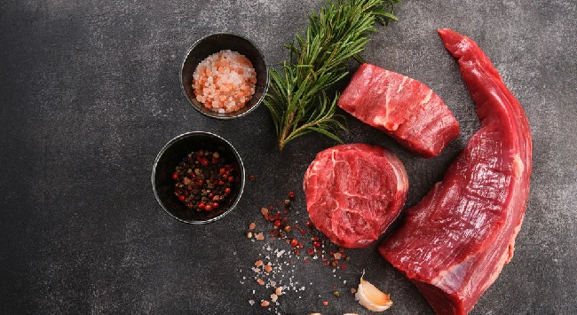 Corte de carne peixinho cru disposto em uma mesa preta com temperos ao lado.